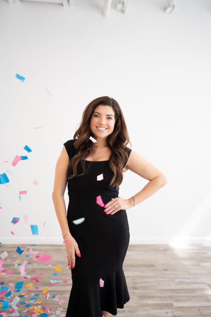 A woman in black dress standing next to wall with confetti.